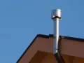 Scarico scaldabagno a gas in facciata, un tubo metallico lucido che sale verso il cielo azzurro, fissato al muro di un edificio.