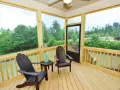 A screened-in porch with two Adirondack chairs, a small table, and a green lantern. The porch offers a view of lush trees and a suburban landscape.