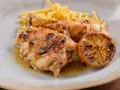 Delicioso pollo al limón con papas fritas crujientes y una rodaja de limón caramelizada.