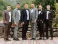 Sześciu mężczyzn w garniturach i białych koszulach, każdy z muszką. Różne kolory i wzory garniturów pokazują, jaka koszula do garnituru pasuje najlepiej.