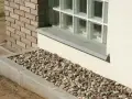 Kamienna opaska żwirowa wokół domu, otaczająca betonową rabatę z kolorowych kamieni, stanowi estetyczne i praktyczne wykończenie.
