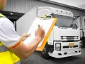 Pracownik w kamizelce odblaskowej wypełnia dokumentację transportową przy białej ciężarówce.