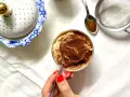 Deliziosa crema al caffè in bicchiere, cosparsa di cacao. Accanto, un elegante contenitore bianco e oro e un cucchiaino con cacao.