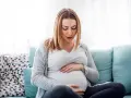 Kobieta w ciąży z rękami na brzuchu, zmartwiona, zastanawia się, jak rozpoznać skurcze porodowe.