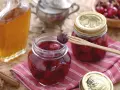 Frascos de mermelada de cerezas casera, una botella de licor y canela en rama. Una cereza en un tenedor de madera lista para probar.