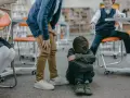 Chłopiec, dziecko wysoko wrażliwe w szkole, siedzi na podłodze, przytulając się. Inni chłopcy stoją nad nim.