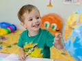 Uśmiechnięte polskie dziecko w hiszpańskiej szkole bawi się globusem i rysuje w zeszycie.