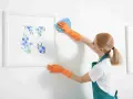 Une femme en gants orange nettoie le cadre d'un tableau de fleurs bleues. Quel produit pour nettoyer un tableau peint à l'huile ?
