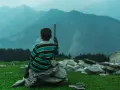 Junge sitzt auf Steinen, blickt in nebelverhangene Berge. Ein Stock in der Hand, wie für einen meditationstext zum vorlesen.