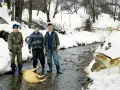 Trzech mężczyzn, w tym Jan Brykczyński, stoi nad strumieniem w śniegu, obok leży świnia. Psy obserwują scenę.