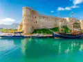 Zamek Kyrenia na Cyprze Północnym z łodziami przycumowanymi w turkusowej zatoce.