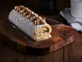 Un delicioso brazo de gitano cubierto de azúcar glas y decorado con crema de café y virutas de chocolate, listo para ser servido.