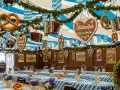Wnętrze namiotu na Oktoberfest w Monachium. Wiszące precle, serca z piernika i akordeony. Stoły przykryte niebiesko-białymi obrusami, ozdobione kwiatami i kolejnymi preclami.
