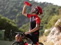 Kolarz w kasku i stroju sportowym pije wodę z bidonu, regenerując siły po wysiłku. Woda z izoleucyną pomoże mu szybciej odzyskać energię.