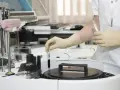 Laborantka w rękawiczkach umieszcza probówkę z próbką do analizy transaminazy GPT w aparaturze laboratoryjnej.
