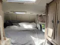 Mysig säng med randigt täcke i en Karmann Mobil. En tygkasse hänger på en krok.