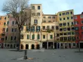 Edifici colorati nel ghetto ebraico di Venezia, con un albero spoglio e una fontana nella piazza lastricata.