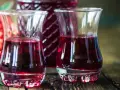 Dwa kieliszki wypełnione rubinową nalewką z czeremchy, obok butelka i kiść owoców.