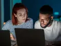 Zwei Personen arbeiten konzentriert an Laptops. Sie besprechen Details, vielleicht für einen partnerschaftsvertrag ohne notar.