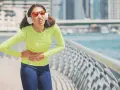 Une coureuse en tenue de sport, écouteurs aux oreilles, se tient le ventre, visiblement prise d'un point de côté.
