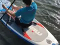 Mann sitzt auf SUP-Board, paddelt und befestigt den Sitz.