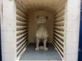 En hundskulptur i blålera keramik väntar på att brännas i en ugn.