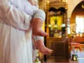Chrzestna trzyma dziecko w kościele. W tle widać ikonostas i ławki.