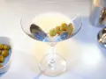 Kto wybierze Dirty Martini czy klasyczne Dry Martini? Kieliszek z oliwkami i drinkiem na białym tle.