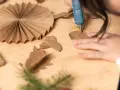 Manos creando manualidades con cartón para adultos. Se usa una pistola de silicona para pegar piezas de cartón, formando adornos.