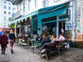 Menschen sitzen an Tischen vor einem **Prenzlauer Berg Restaurant** mit türkisfarbener Markise und Graffiti.