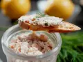 Un toast garni de rillettes de saumon, décoré d'aneth, avec un pot de rillettes en arrière-plan.