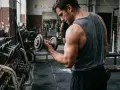 Homme concentré faisant un exercice biceps haltère dans une salle de sport rustique.