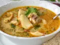 Sopa de pescado casera en un cuenco blanco con trozos de pescado, perejil y una rebanada de pan.