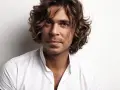Hombre con cabello castaño ondulado, un ejemplo de cortes de pelo hombre medio largo, viste camisa blanca.