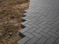 Pavimentazione in autobloccanti grigi posati a spina di pesce, con bordo a vista sulla terra. Valuta il costo autobloccanti al mq per il tuo progetto.