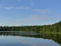 Idyllischer Bullensee in Rotenburg, umgeben von dichtem grünen Wald, spiegelt sich im ruhigen Wasser unter blauem Himmel mit Wolken.