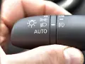 Dłoń naciska przełącznik świateł w samochodzie, wybierając tryb AUTO, który może obejmować światła do jazdy dziennej (DRL).