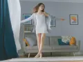 Frau tanzt im Wohnzimmer, die Gardinen wehen. Sie fragt sich, wie oft Gardinen waschen, um die Frische zu bewahren.