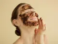 Mujer disfrutando de una mascarilla de café para la cara, con los ojos cerrados y una sonrisa.