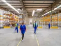 Persone in movimento in un magazzino moderno, con scaffalature piene di merci. Un'immagine che evoca il dinamismo del lavorare come magazziniere.