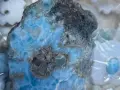 Surowy larimar, kamień o niebiesko-białych żyłkach, otoczony perłami i ozdobami. Jego magiczne właściwości uspokajają i przynoszą harmonię.