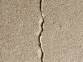 Grosse fissure sur un mur extérieur en crépi. Il faut réparer cette fissure pour éviter qu'elle ne s'aggrave.