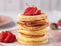 Pancakes dorati, perfetti per una ricetta pancake veloce senza lievito, guarniti con fragole fresche e zucchero a velo.