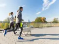 Coppia che corre con il cane su un ponte in una giornata di sole.
