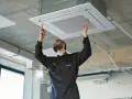 Técnico ajustando una unidad de cassette para la instalación de ventilación en un techo de hormigón.