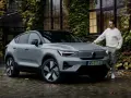Szary Volvo C40 z czarnym dachem stoi na mokrej, brukowanej nawierzchni. Mężczyzna w białym swetrze opiera się o maskę.