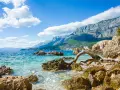Piękne wybrzeże Chorwacji z turkusową wodą, skalistą plażą i górzystym krajobrazem w tle. Idealne miejsce, by zastanowić się, gdzie do Chorwacji.