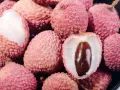 Stos świeżych liczi, jeden przekrojony, ukazujący biały miąższ i brązową pestkę.