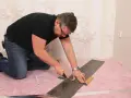 Mann kniet und schneidet mit einem Cuttermesser und Lineal eine Diele für den vinylboden verlegen.