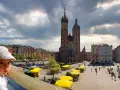 Małe dziecko w czapce patrzy na Rynek Główny w Krakowie, gdzie znajdują się liczne atrakcje dla dzieci w krakowie, w tym kramy z żółtymi parasolami.